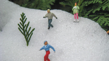 Close-up of brightly-coloured vintage figurines wearing ice skates, arranged on snow piled to look like a ski hill