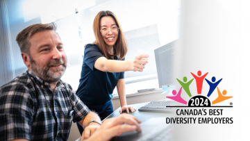 Two smiling staff look at a computer monitor, logo "2024 Canada's Best Diversity Employers"