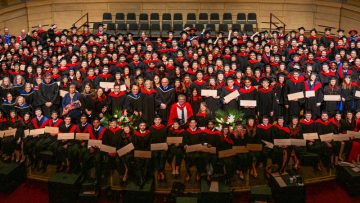 Group photo of Dean Dermot Kelleher and new graduates on stage following the 2025 MD Hooding Ceremony