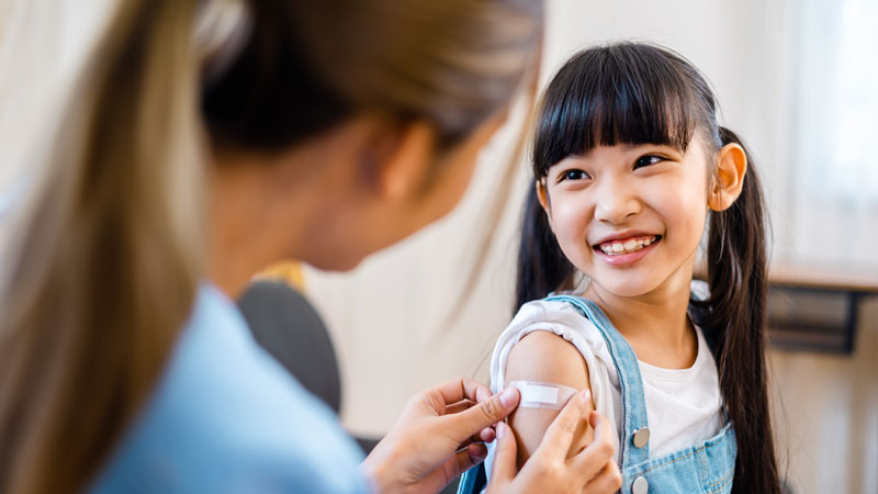 A healthcare worker puts an adhesive bandage on a smiling girl's arm